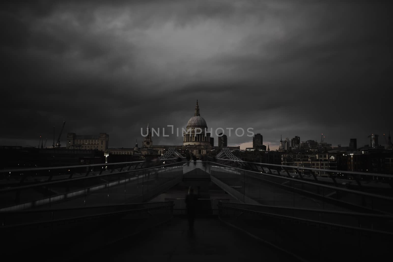 Millennium Bridge ramp with the St Paul Cathedral in the distance below creepy-looking cloudy sky. Dark gray skyline above British cathedral during dusk. Dark London cityscapes