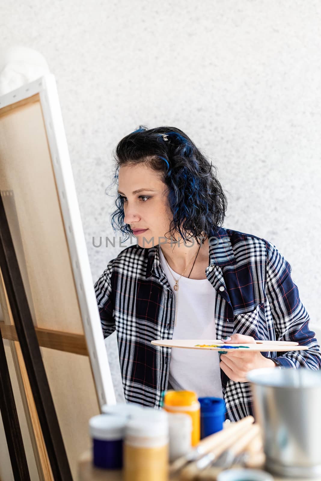 Creative woman with blue dyed hair painting in her studio by Desperada