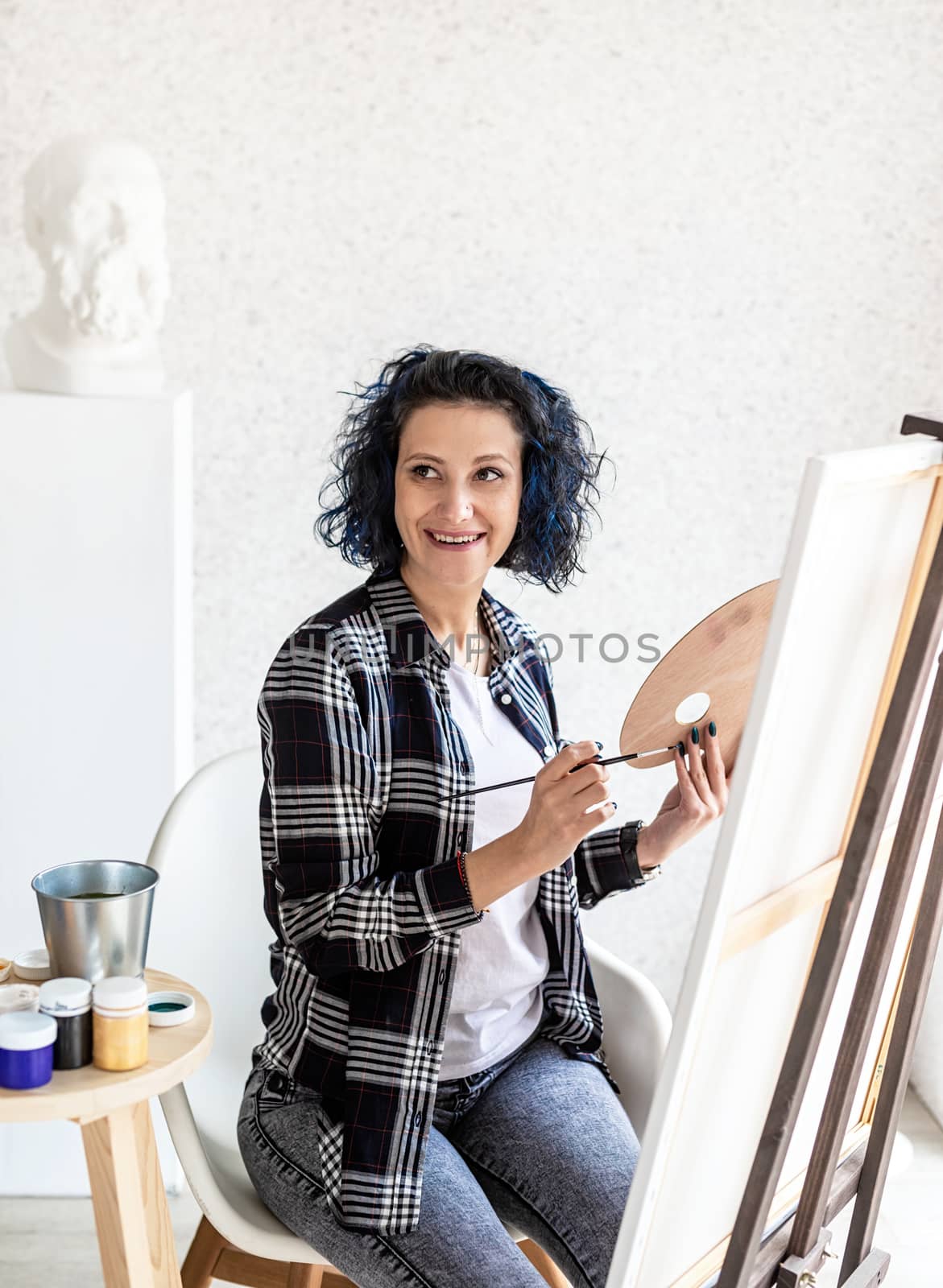 Creative woman with blue dyed hair painting in her studio by Desperada