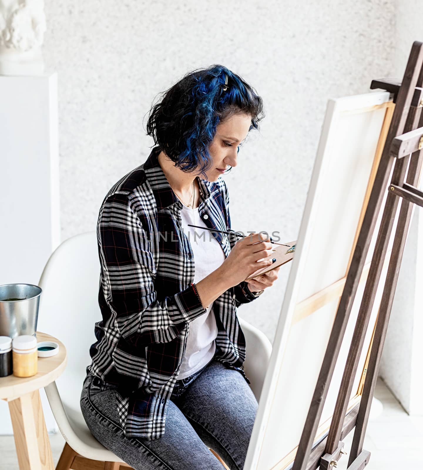 Creative woman with blue dyed hair painting in her studio by Desperada