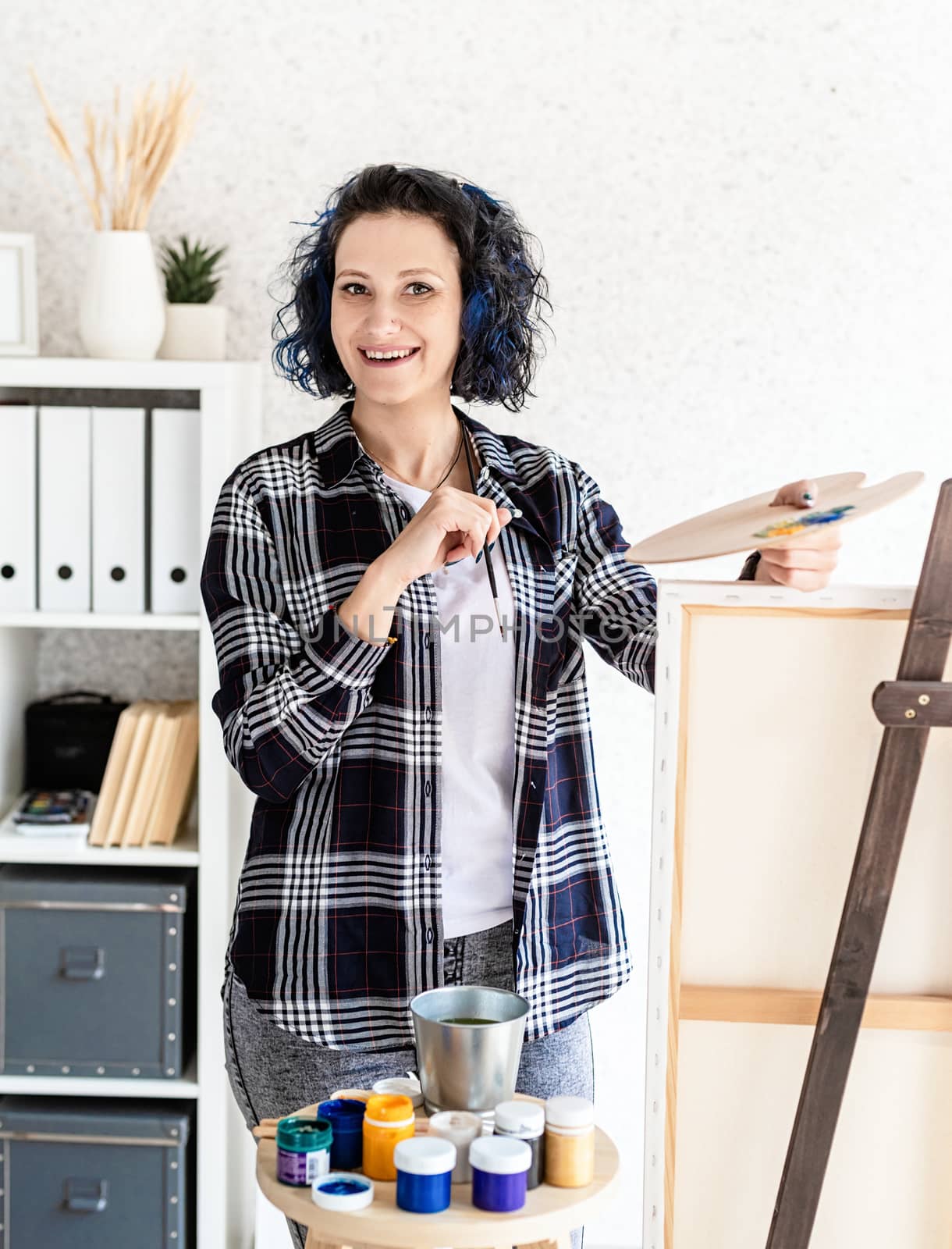 Creative woman with blue dyed hair painting in her studio by Desperada