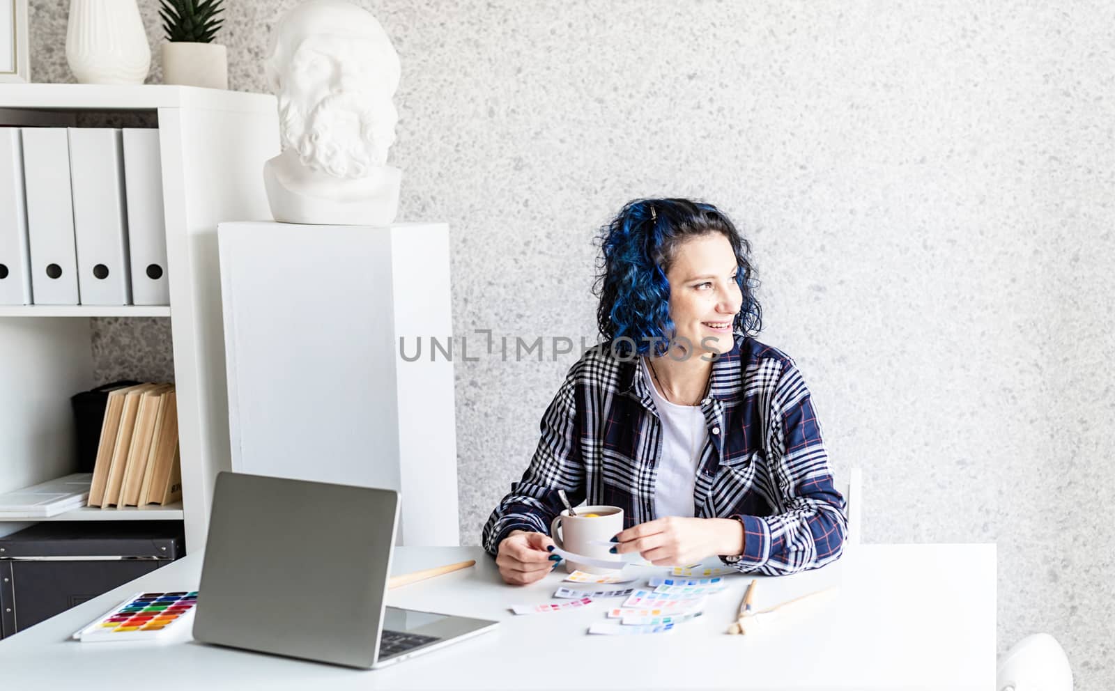 Designer working with colour palettes and laptop in her art studio