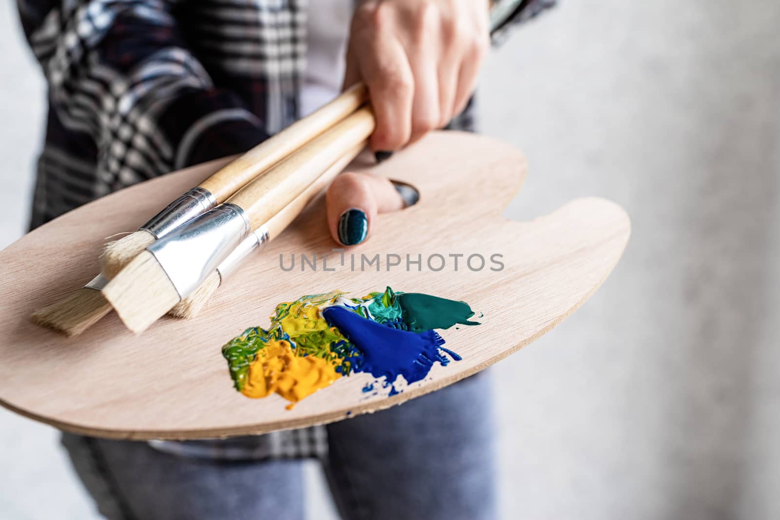 Close up of artist hands holding wooden art palette and paintbrushes by Desperada