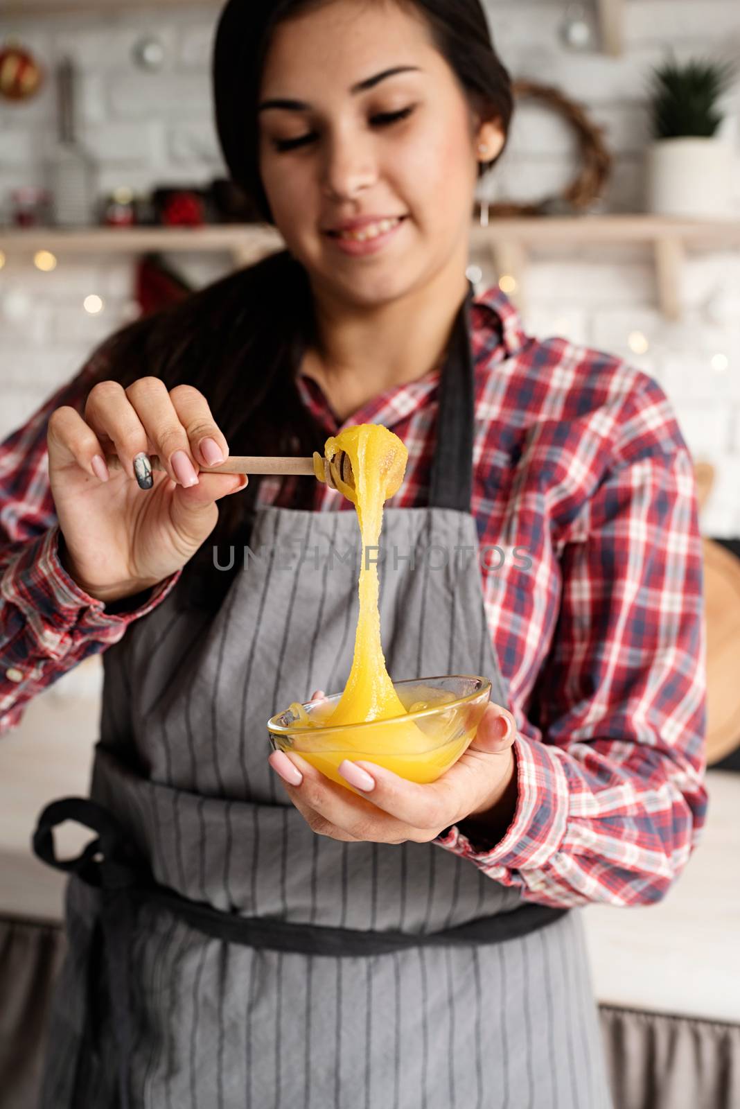 Young latin woman pouring the honey to the dough cooking at the kitchen by Desperada