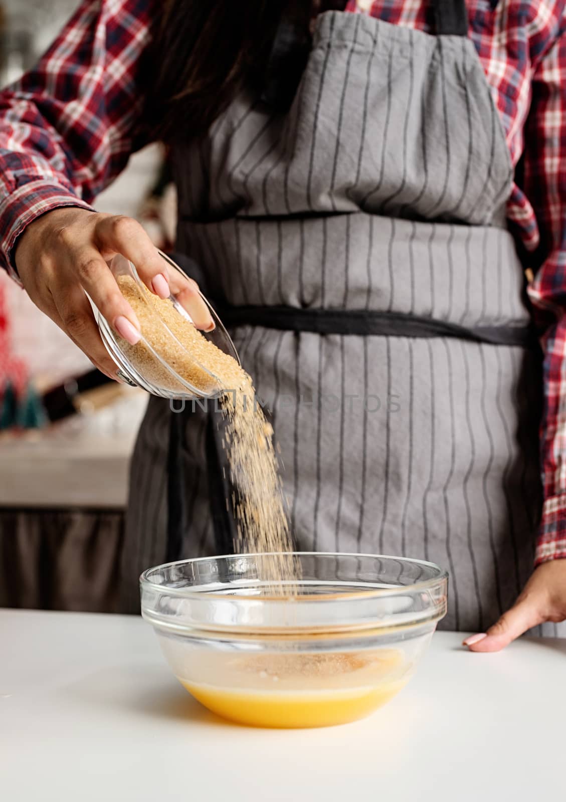 Young latin woman pouring sugar to the dough cooking at the kitchen by Desperada