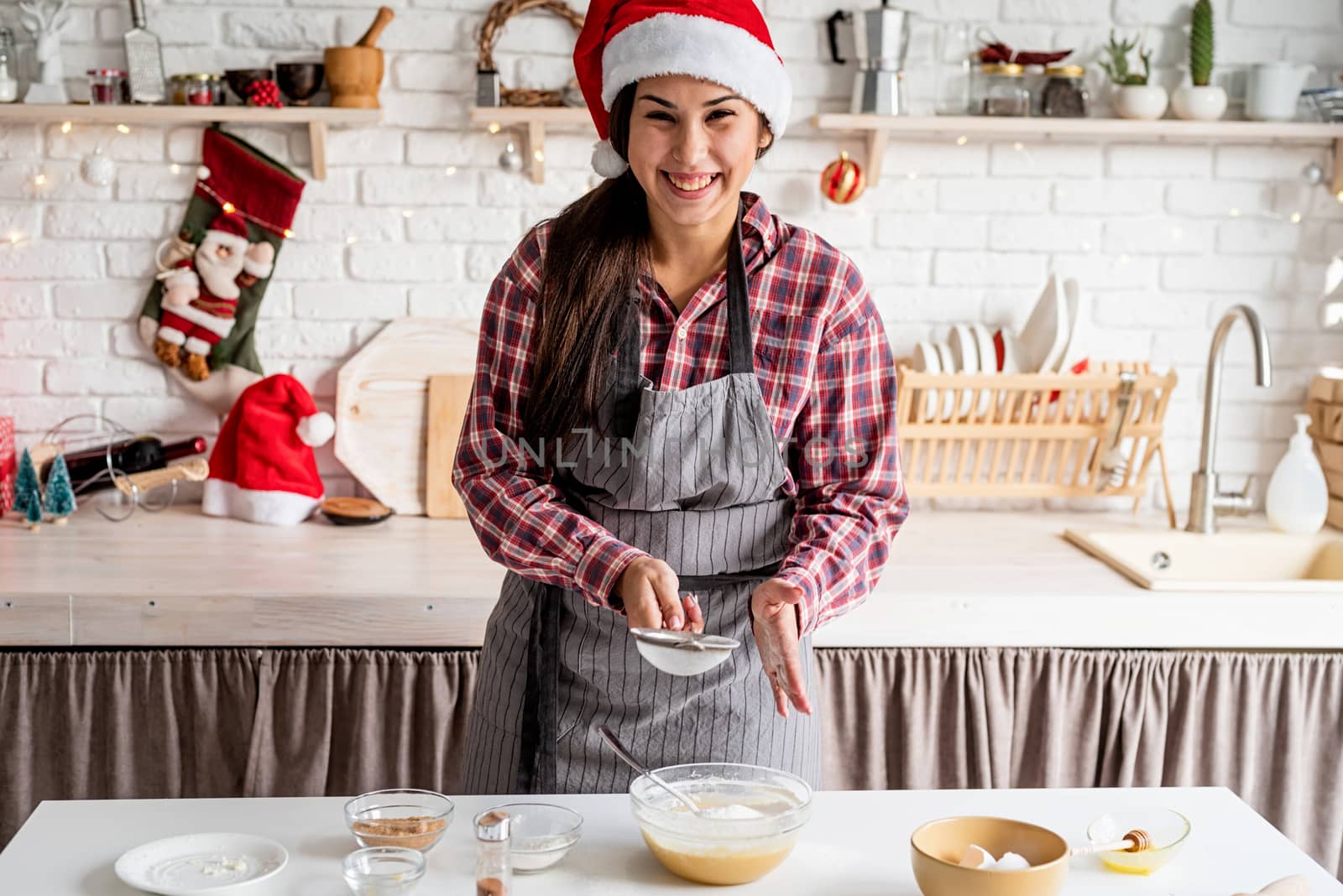 Young latin woman pouring flour to the dough cooking at the kitchen by Desperada