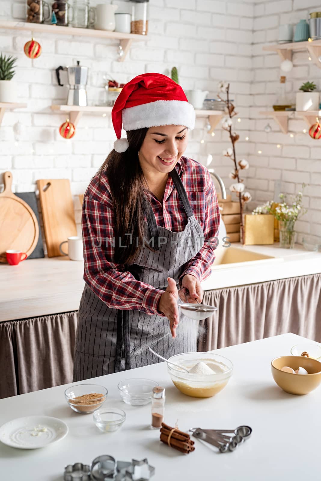 Young latin woman pouring flour to the dough cooking at the kitchen by Desperada