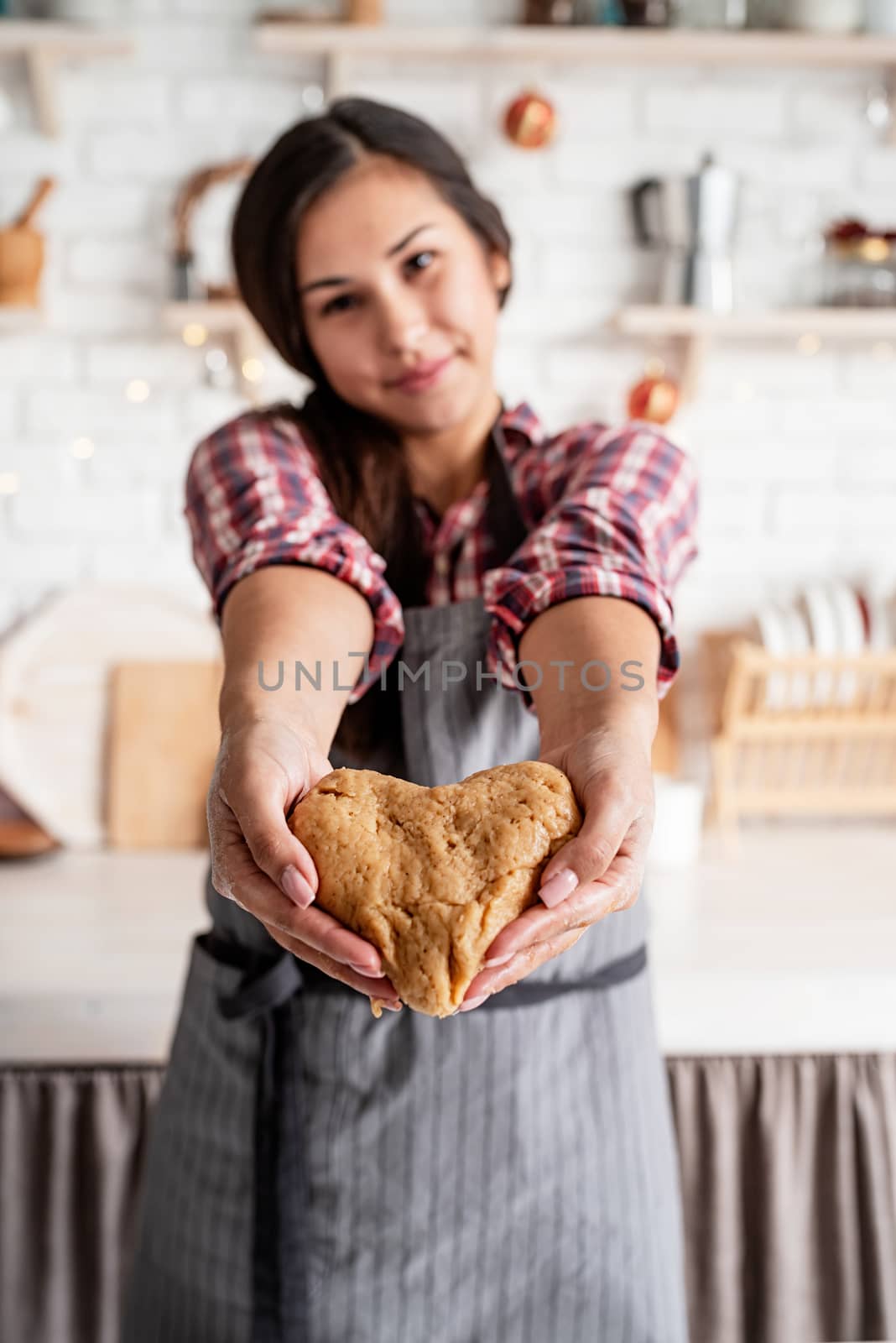 Cooking and baking. Happy brunette woman holding heart shaped dough at the kitchen