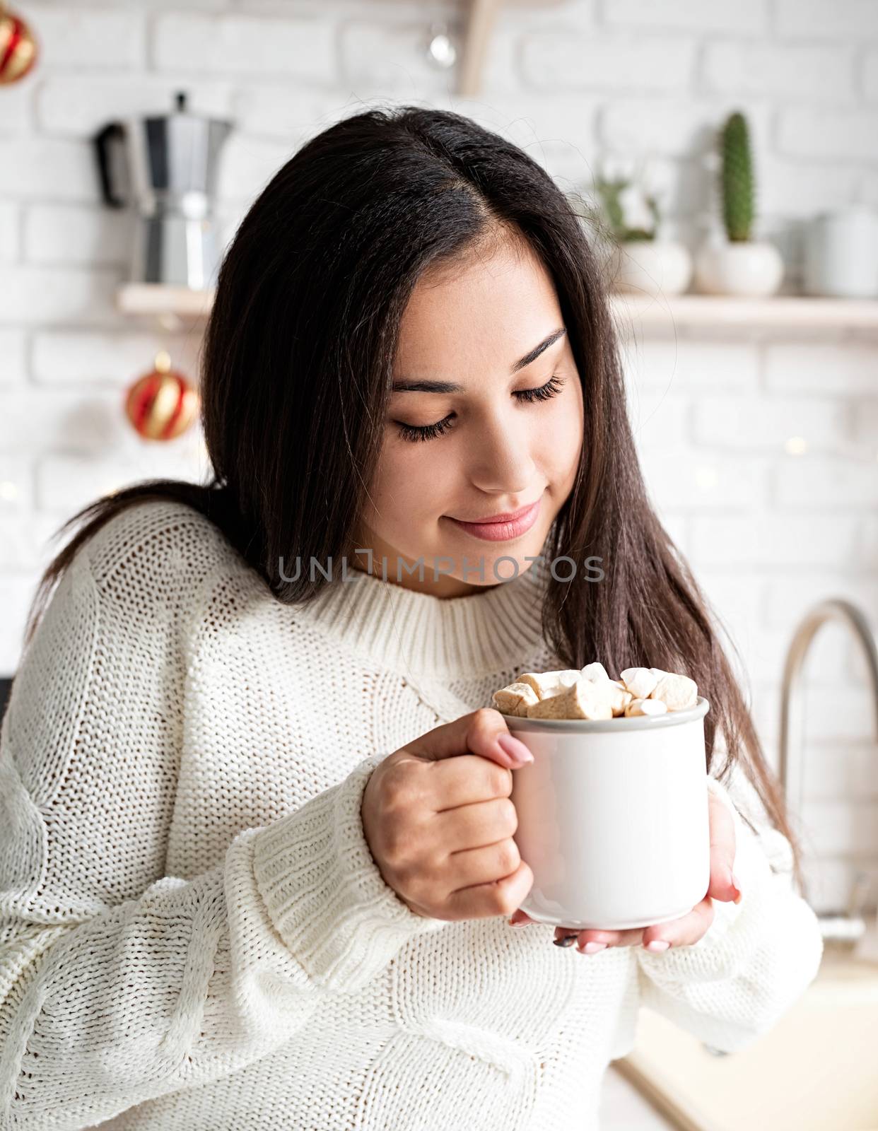 Brunette woman holding a cup of marshmallow cocoa in the kitchen by Desperada