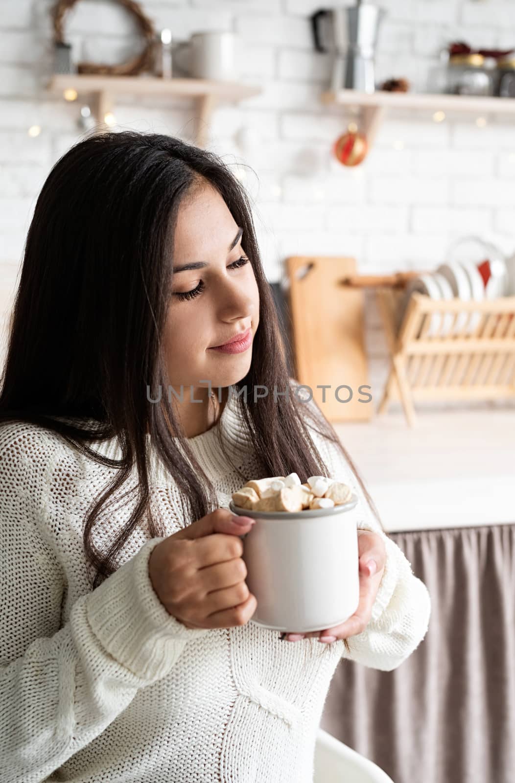 Brunette woman holding a cup of marshmallow cocoa in the kitchen by Desperada