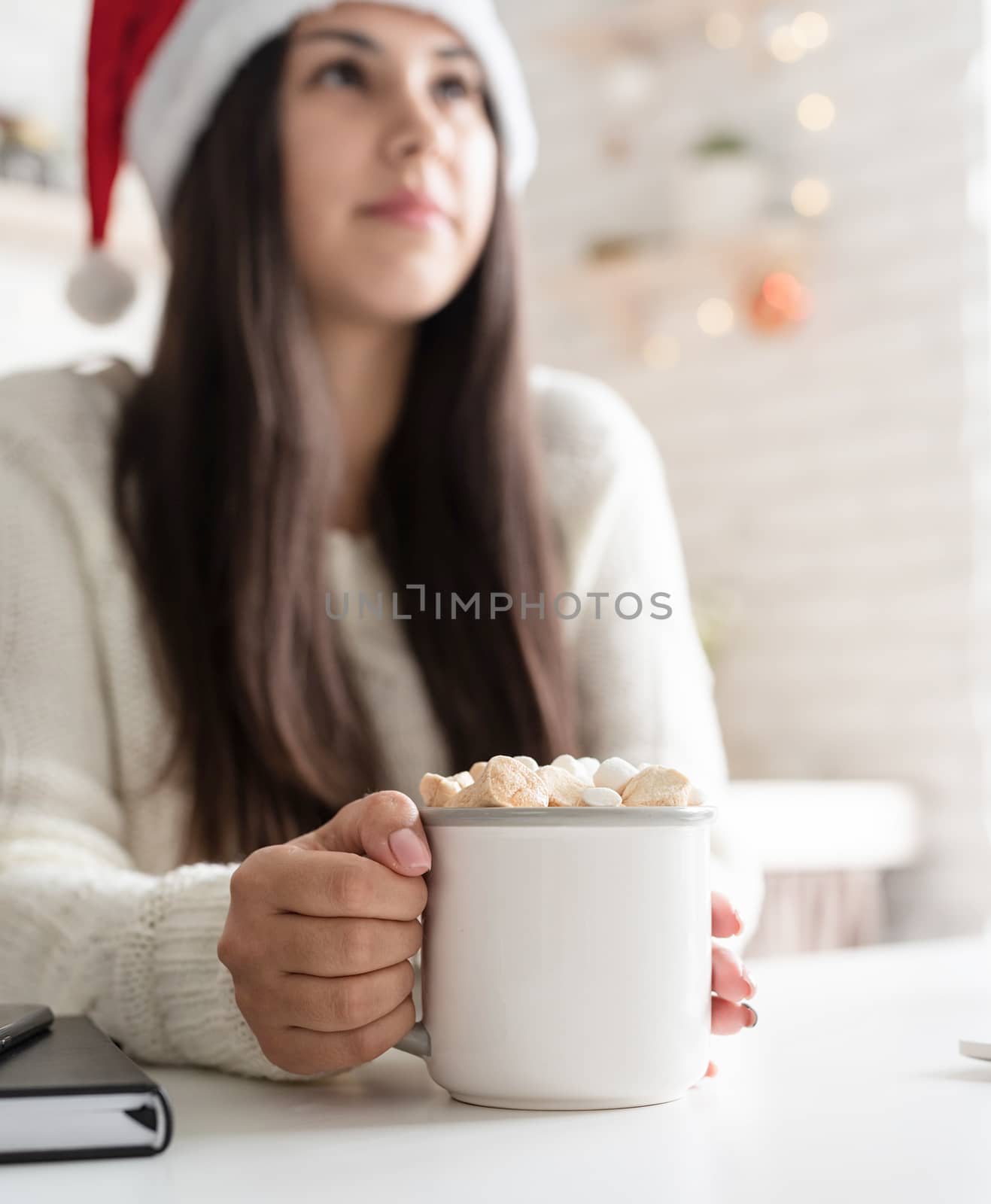Christmas and New Year. Brunette woman in santa hat holding a cup of marshmallow cocoa