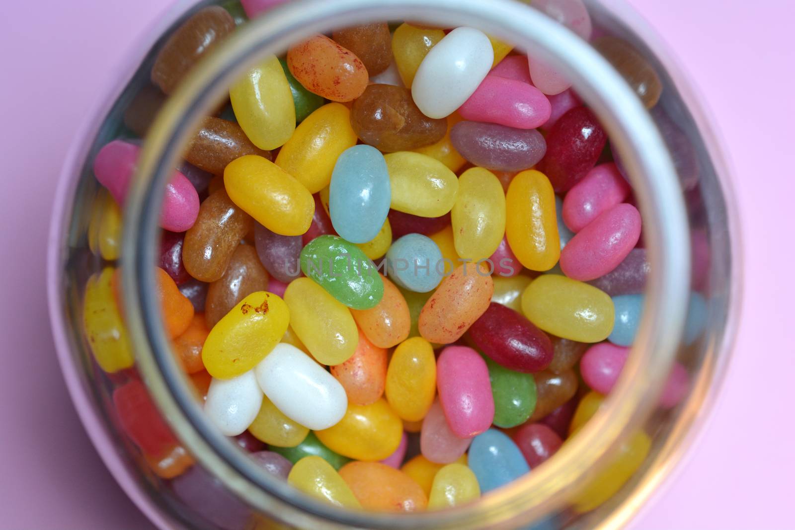 Top view of a glass jar filled with jelly beans on pink background