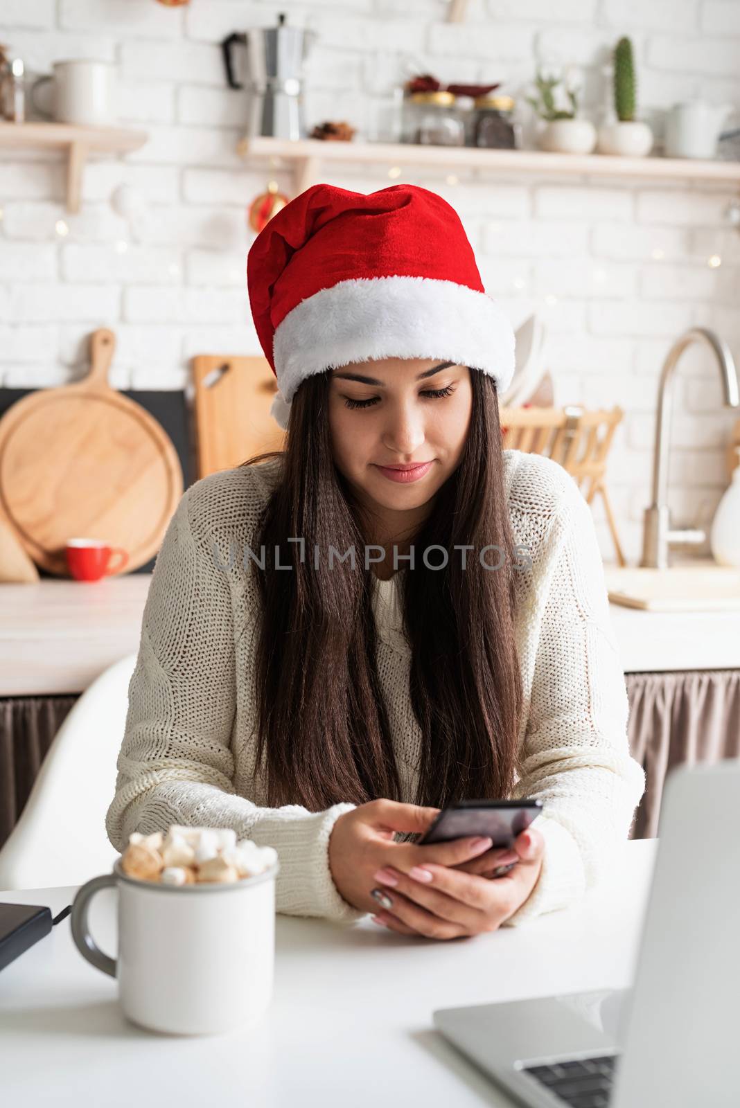 Christmas and New Year. Young brunette woman chatting with friends using her mobile phone at the kitchen