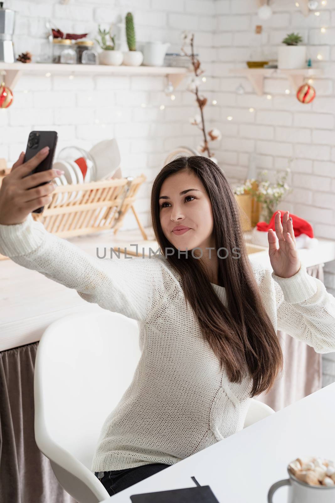 Christmas and New Year. Young brunette woman chatting with friends using her mobile phone at the kitchen