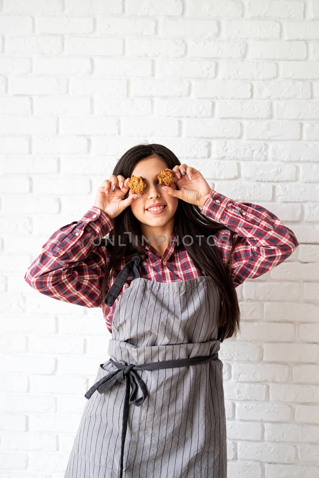 Happy woman in apron holding star shaped cookies in front of her eyes by Desperada