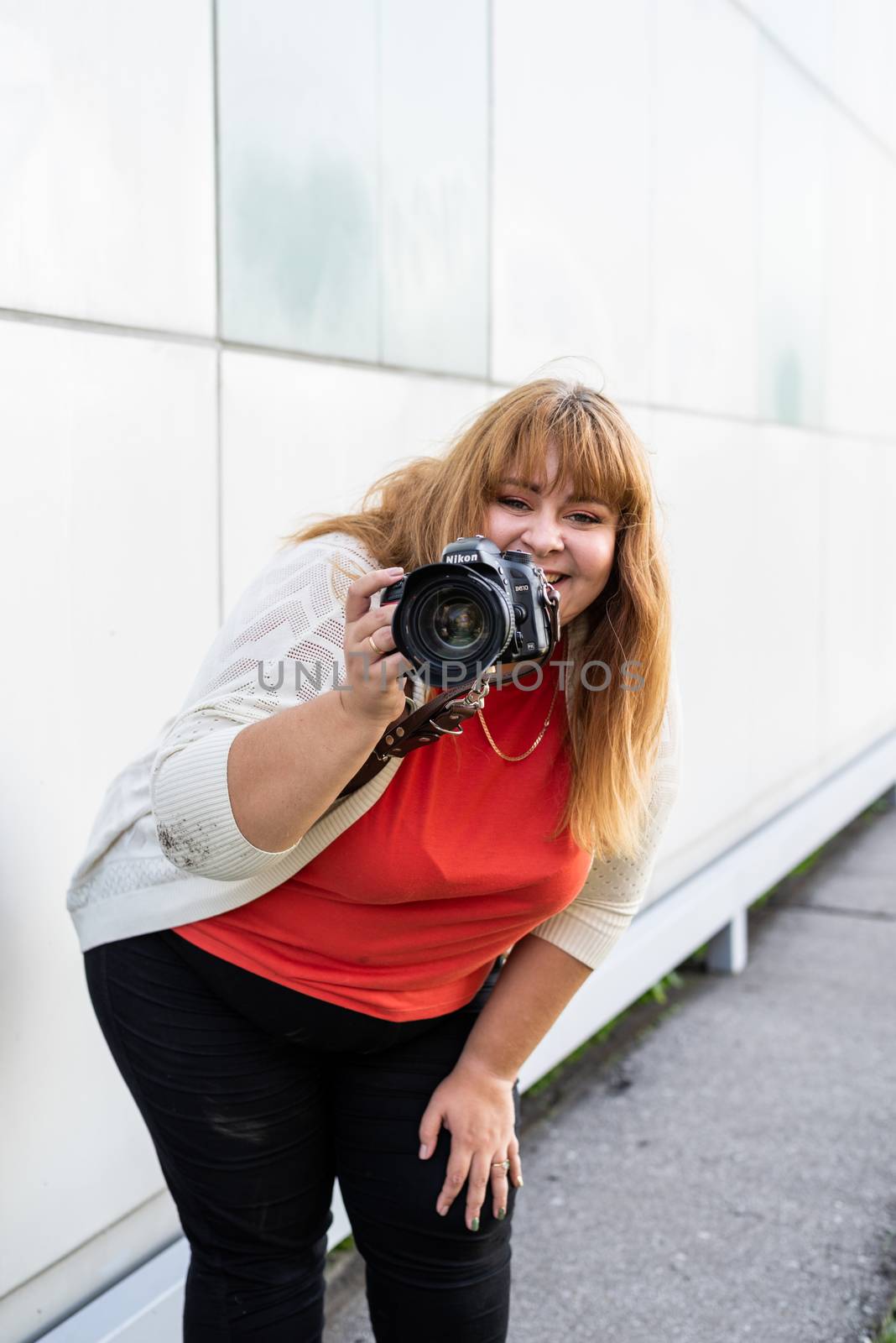 Body positive. Portrait of overweight woman taking pictures with a camera outdoors