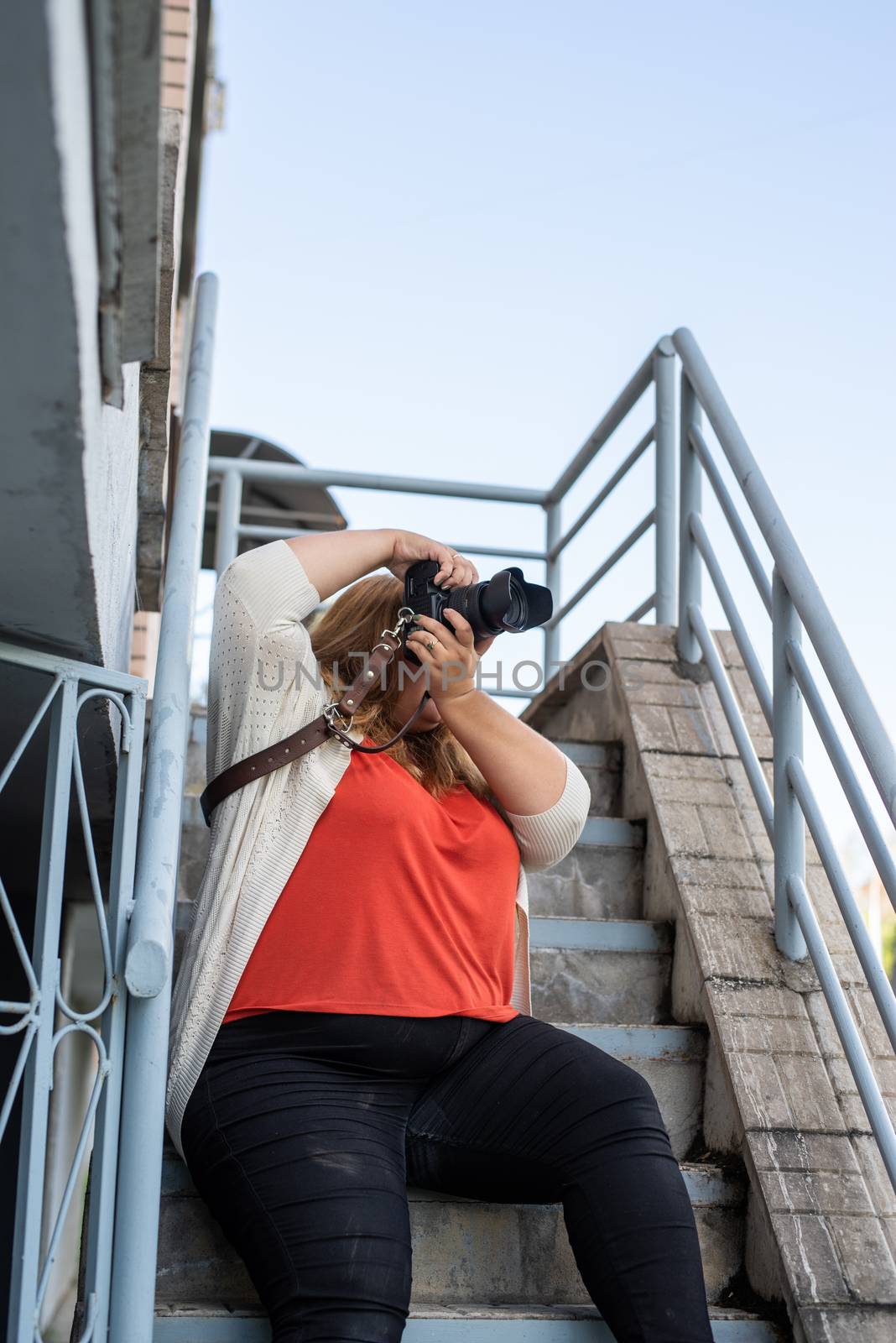 Portrait of overweight woman taking pictures with a camera outdoors by Desperada