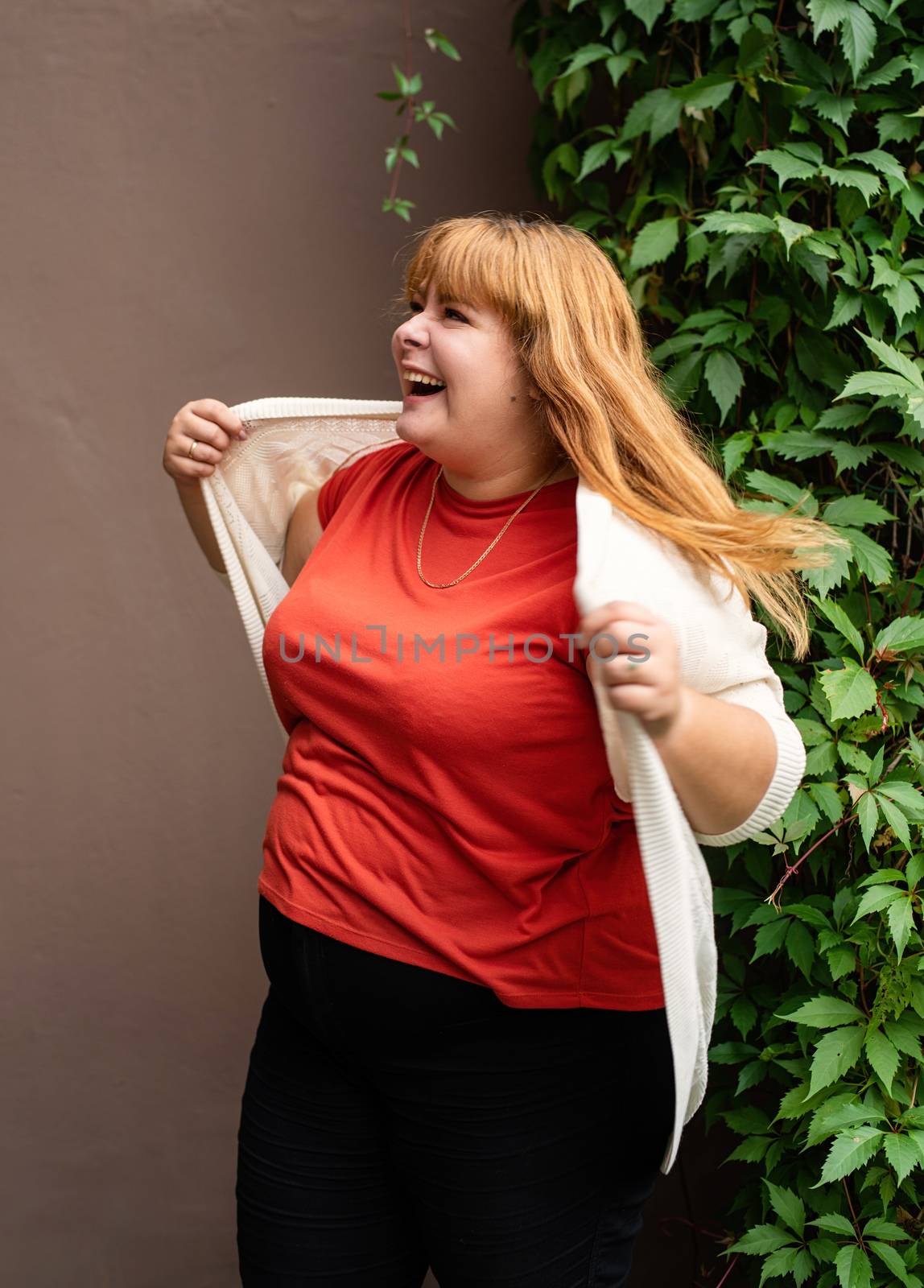 Body positive. Confident overweight woman posing on the brown solid wall on the street