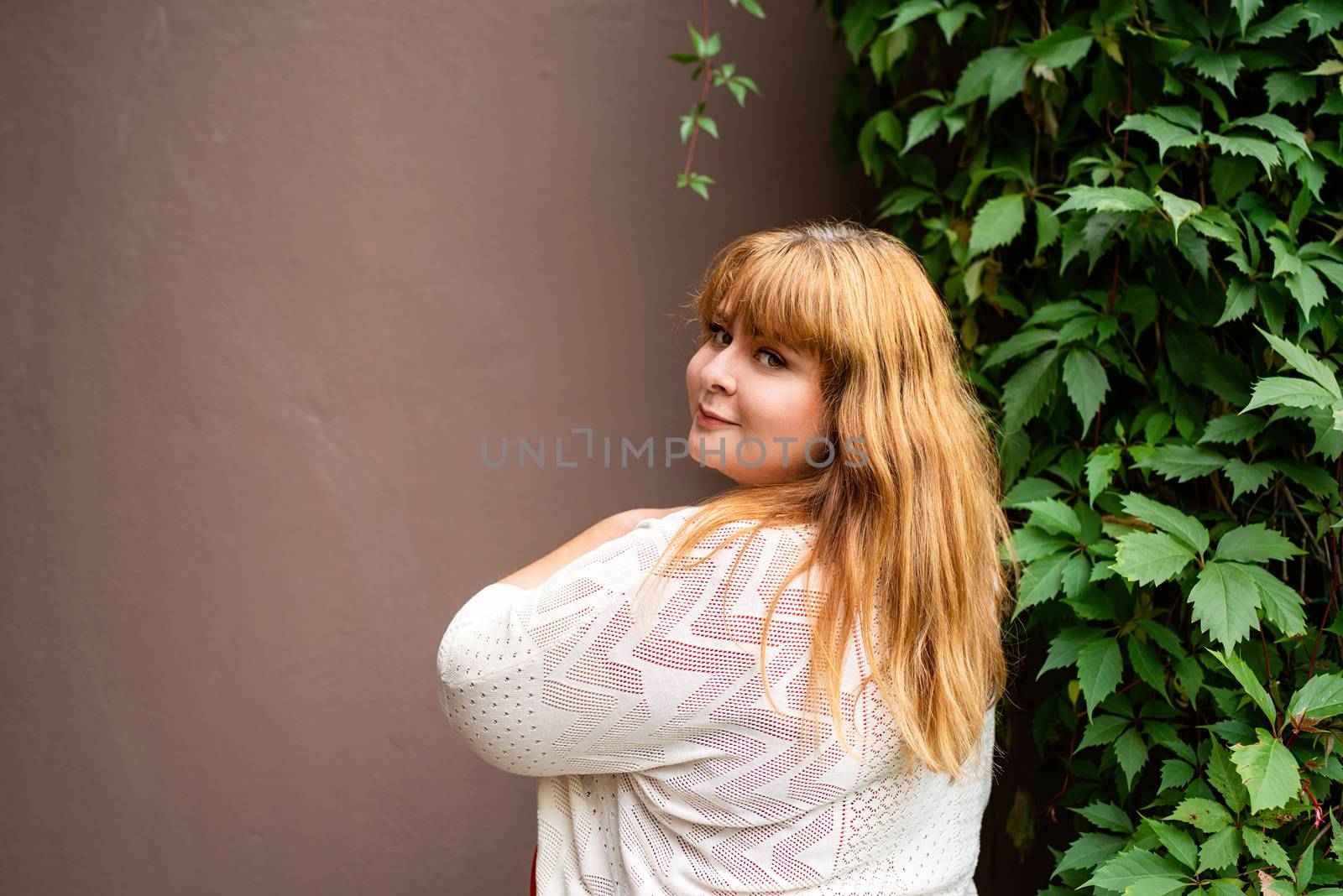 Confident overweight woman posing on the brown solid wall on the street by Desperada
