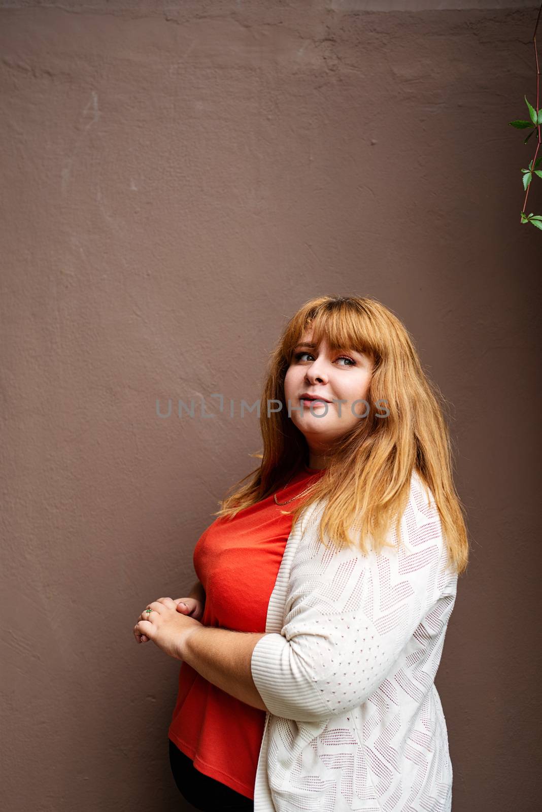 Body positive. Confident overweight woman posing on the brown solid wall on the street