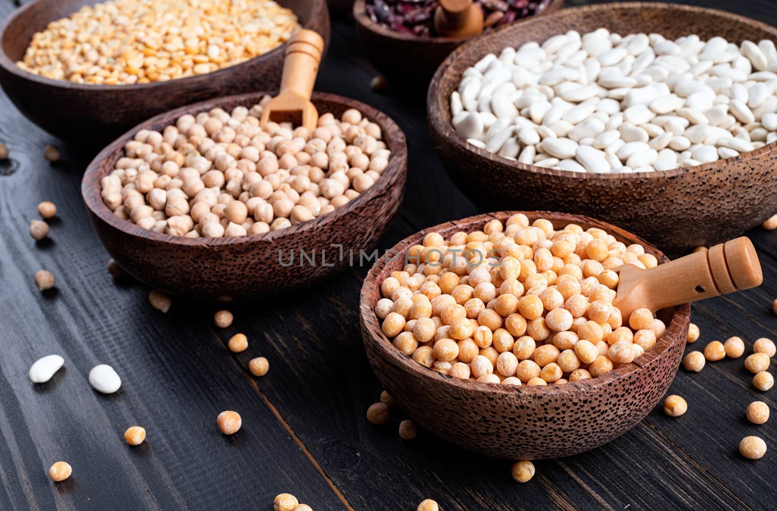 Various dried legumes in wooden bowls on wooden background