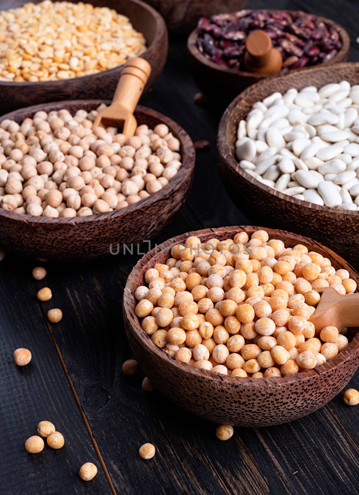 Various dried legumes in wooden bowls on wooden background by Desperada