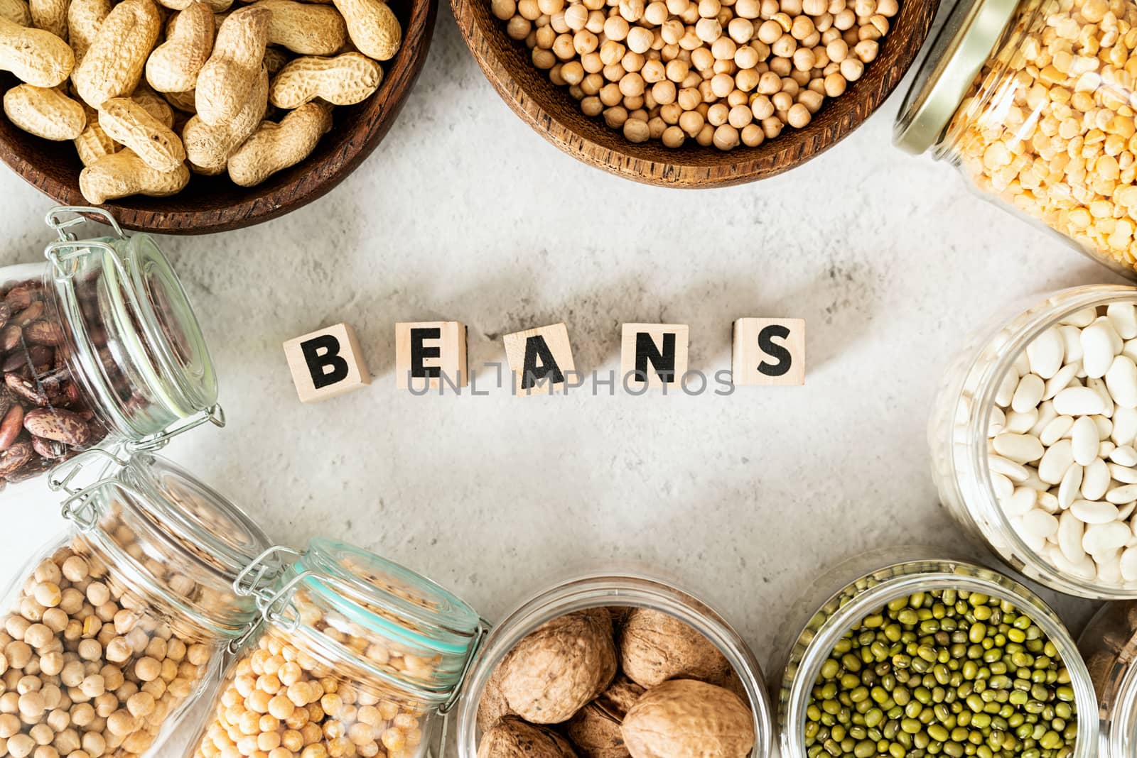 Various dried legumes in wooden bowls with the text Beans top view flat lay on white marble background