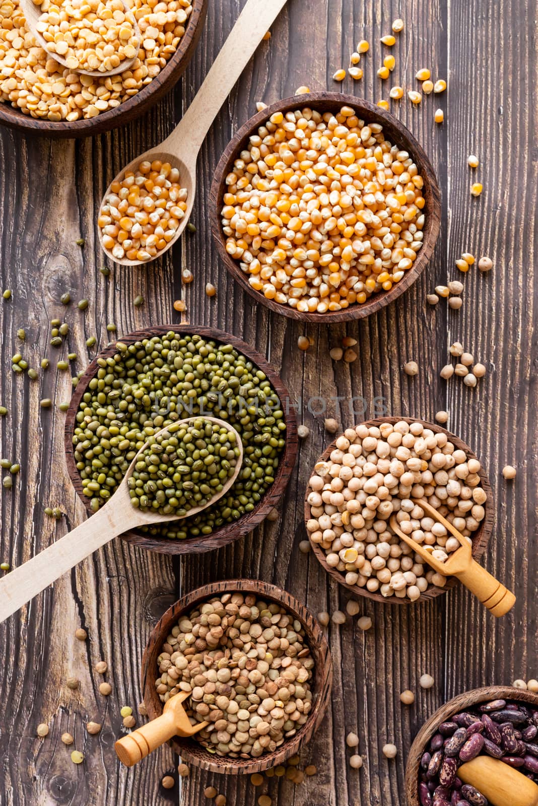 Various dried legumes in wooden bowls top view flat lay on wooden rustic background by Desperada