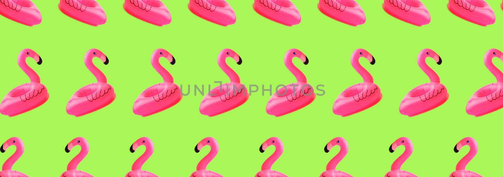 Creative concept of beach and summer vacation.Seamless pattern from inflatable pink mini flamingos on a green background. Floating inflatable flamingo. Flamingo Trend Inflatable Toy.Summer background