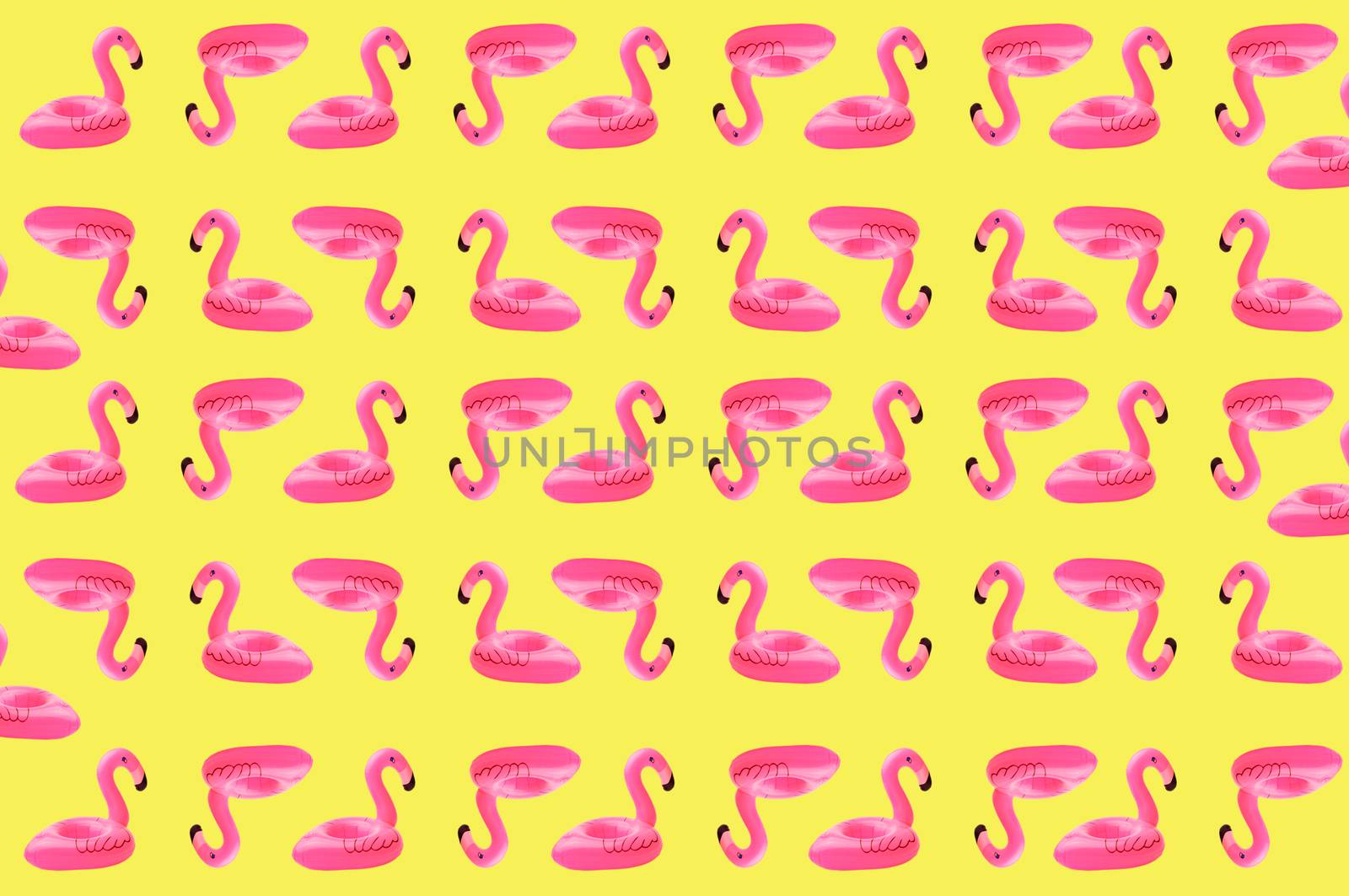 Creative concept of beach and summer vacation.Seamless pattern from inflatable pink mini flamingos on a sandy background.Floating inflatable flamingo. Flamingo Trend Inflatable Toy. Summer background