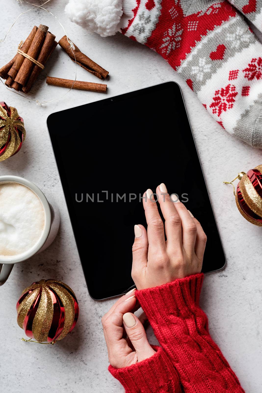 Christmas desktop with woman hands, tablet surrounded by coffee, stockings, decorations top view flat lay