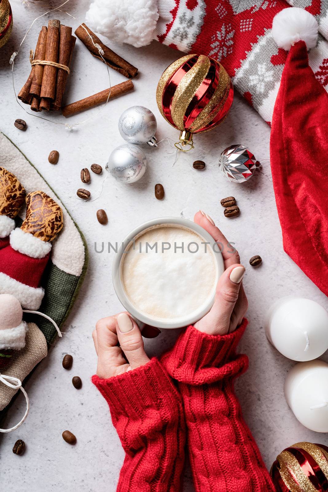 Christmas and New Year. Christmas desktop with woman hands holding a cup of coffee surrounded by decorations, stockings and santa hat top view flat lay