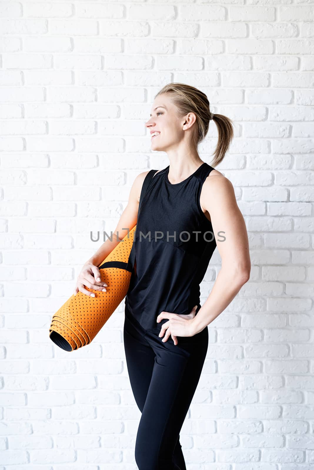 Healthy lifestyle. Sport and fitness. Smiling athletic woman in black sportwear on white brick wall background