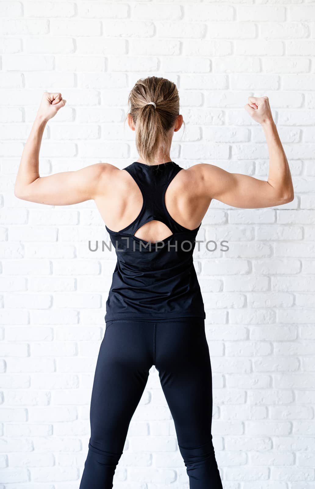 Rear view of an athletic woman in black sportwear showing her back and arms muscles by Desperada