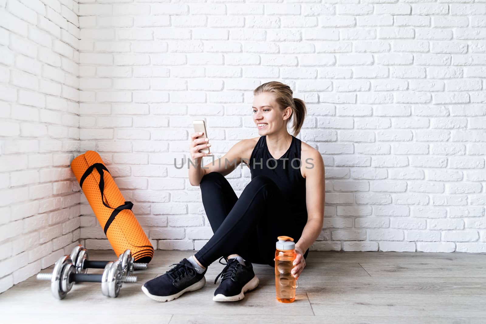 Healthy lifestyle. Sport and fitness. Young smiling fitness woman doing selfie after workout sitting at the floor drinking water