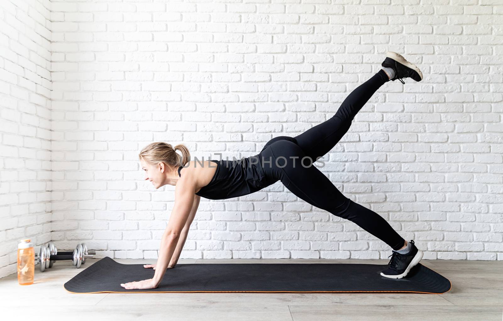 Young fit woman in black sportswear doing push ups at home by Desperada
