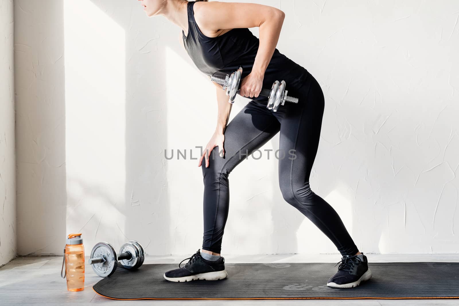 Healthy lifestyle. Sport and fitness. Young blond woman working out doing dumbbell lifts training her back and arms