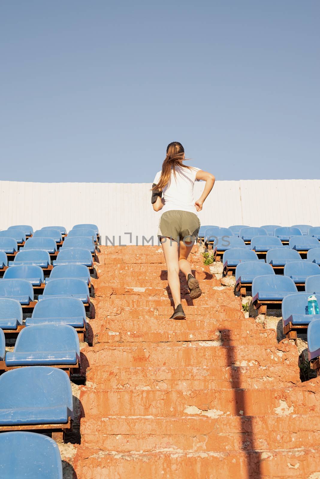 Teenager girl working out at the staduim running up the stairs by Desperada