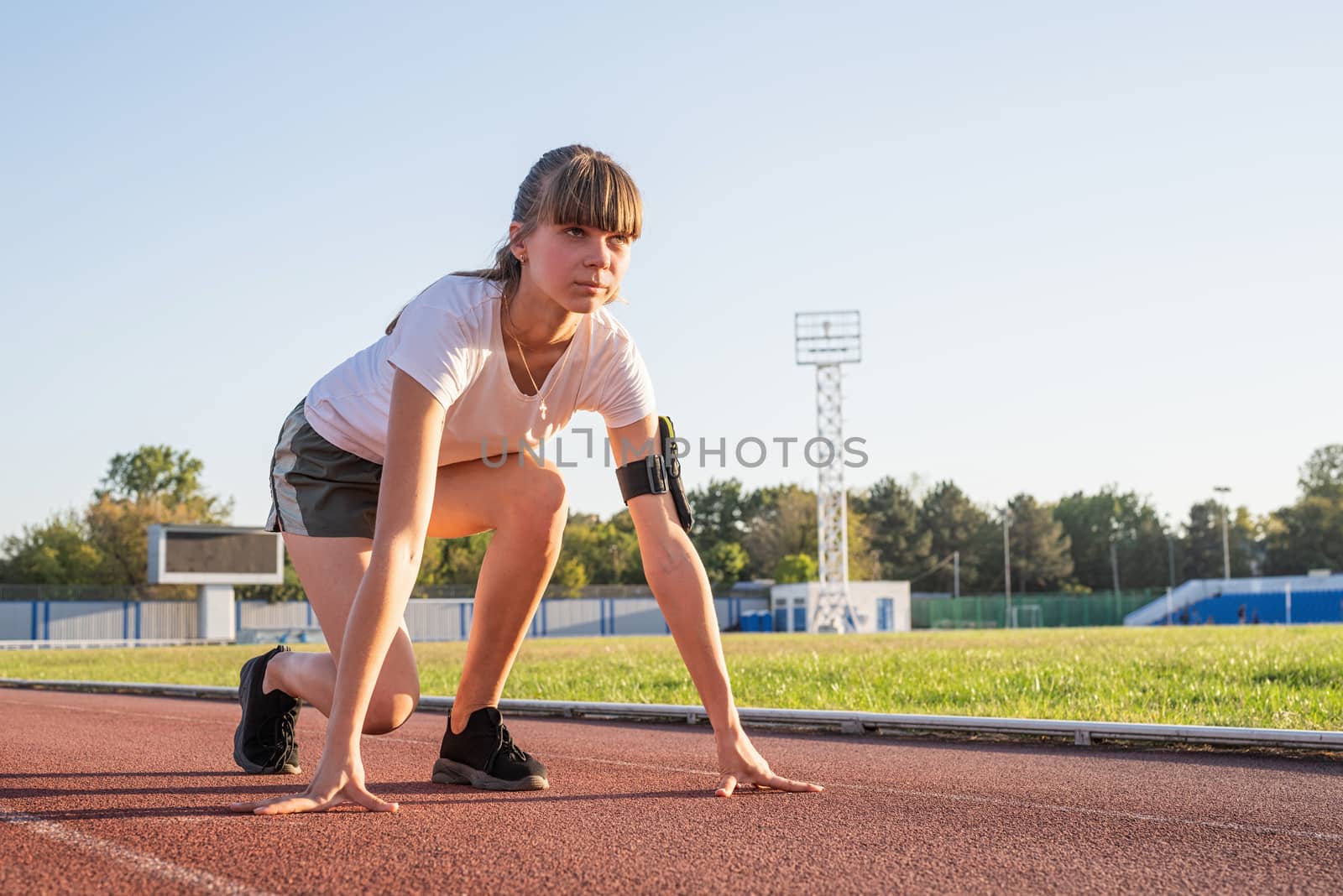 Young woman on starting position, getting ready to run at stadium track by Desperada