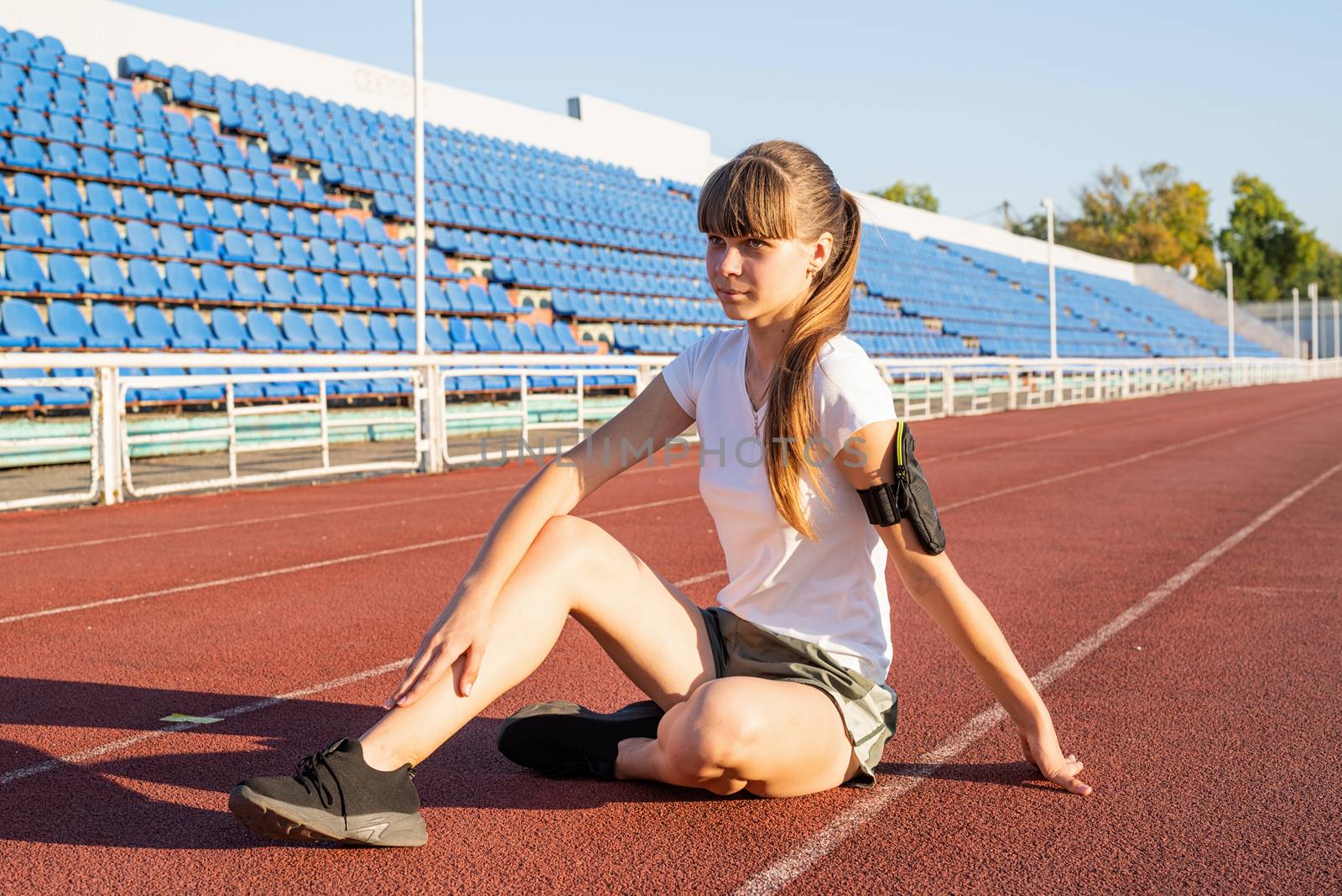Teenager girl sitting on stadium track having rest by Desperada