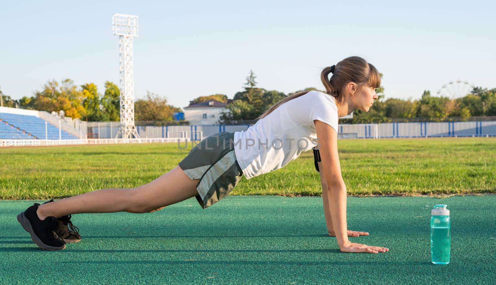 Teenager girl doing workout standing in a plank position at the stadium by Desperada