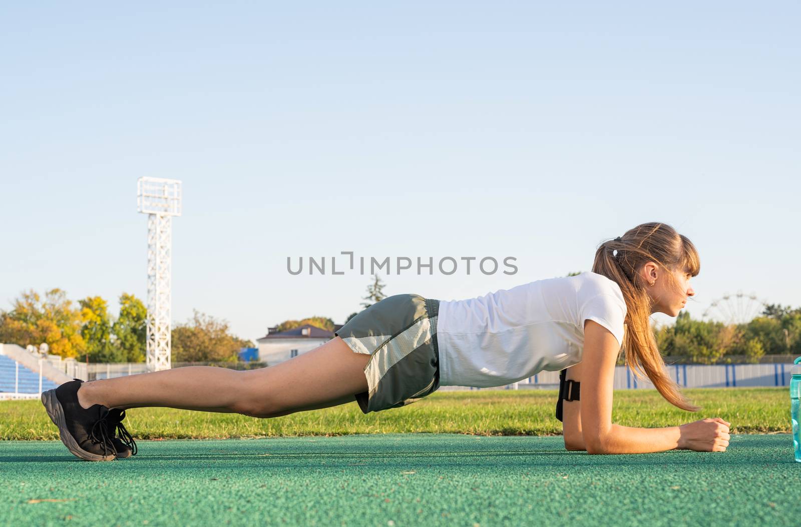 Teenager girl standing in a plank position doing workout at the stadium by Desperada