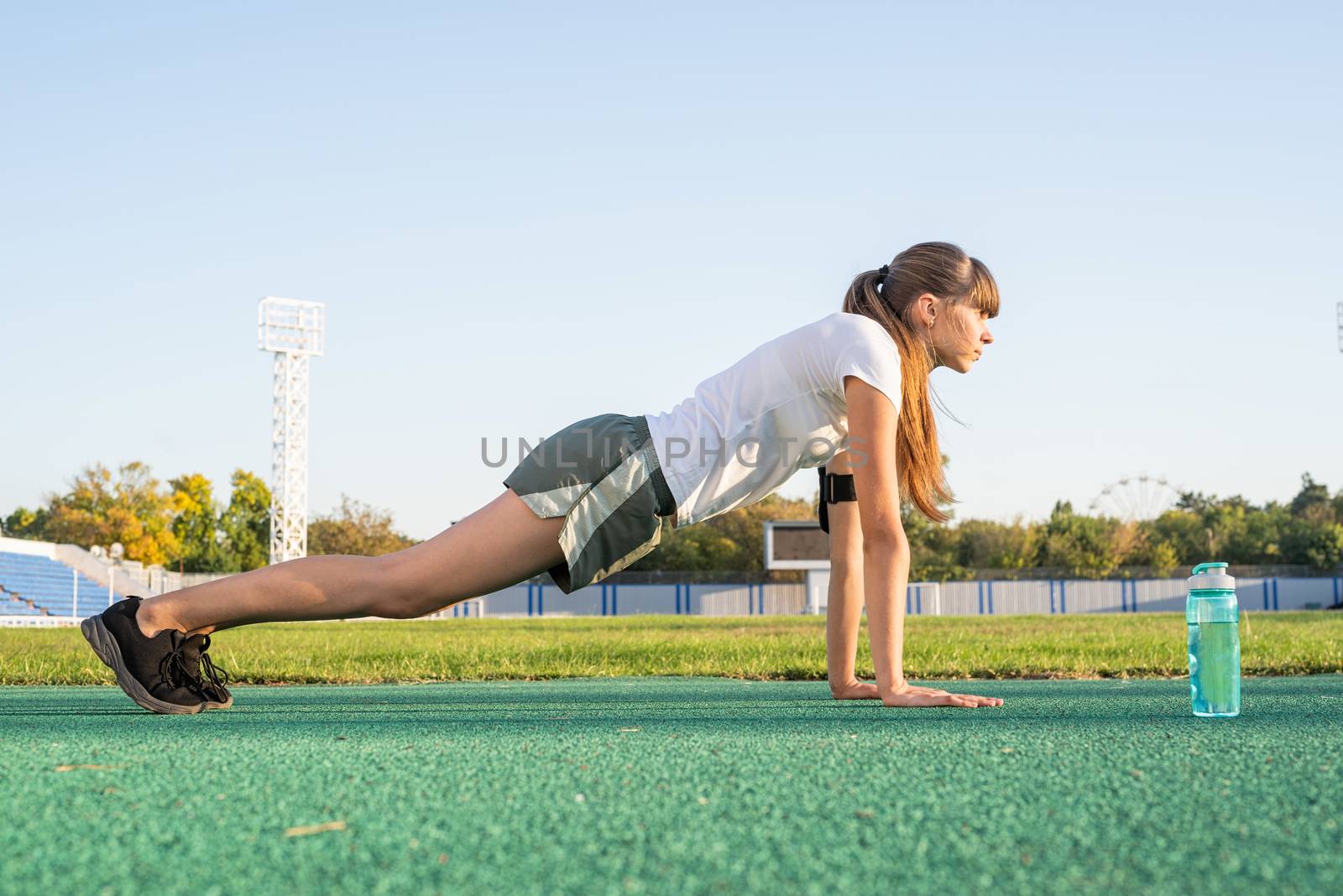 Teenager girl doing workout standing in a plank position at the stadium by Desperada