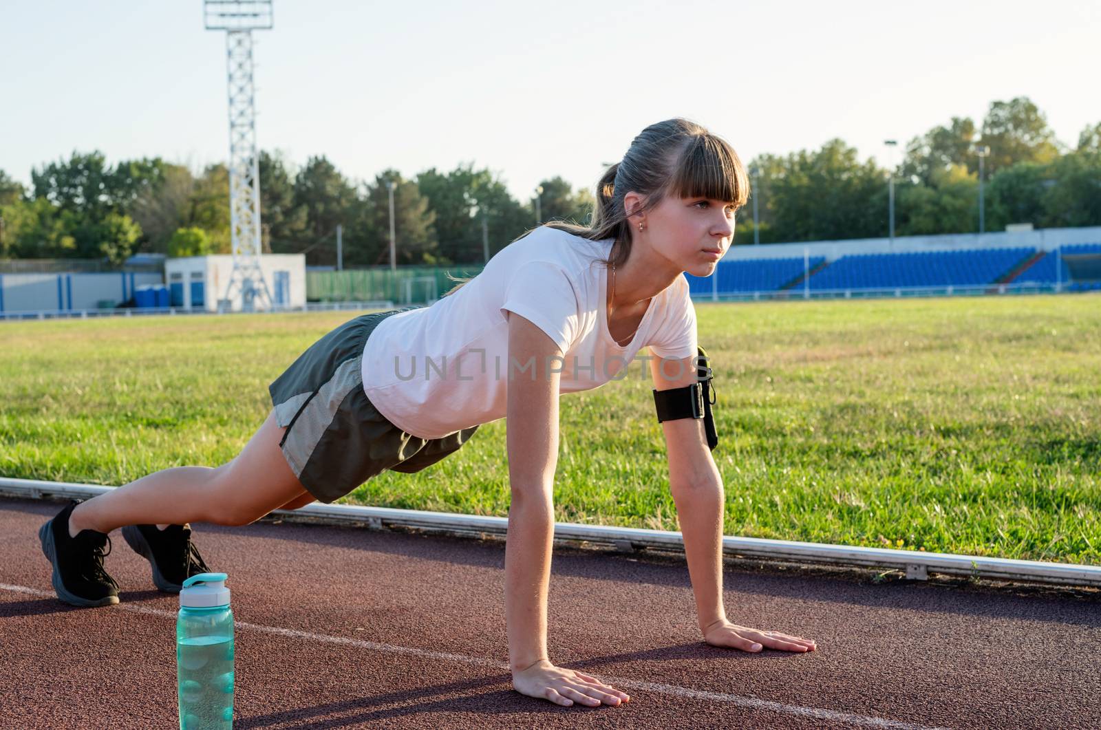 Teenager girl doing workout standing in a plank position at the stadium by Desperada