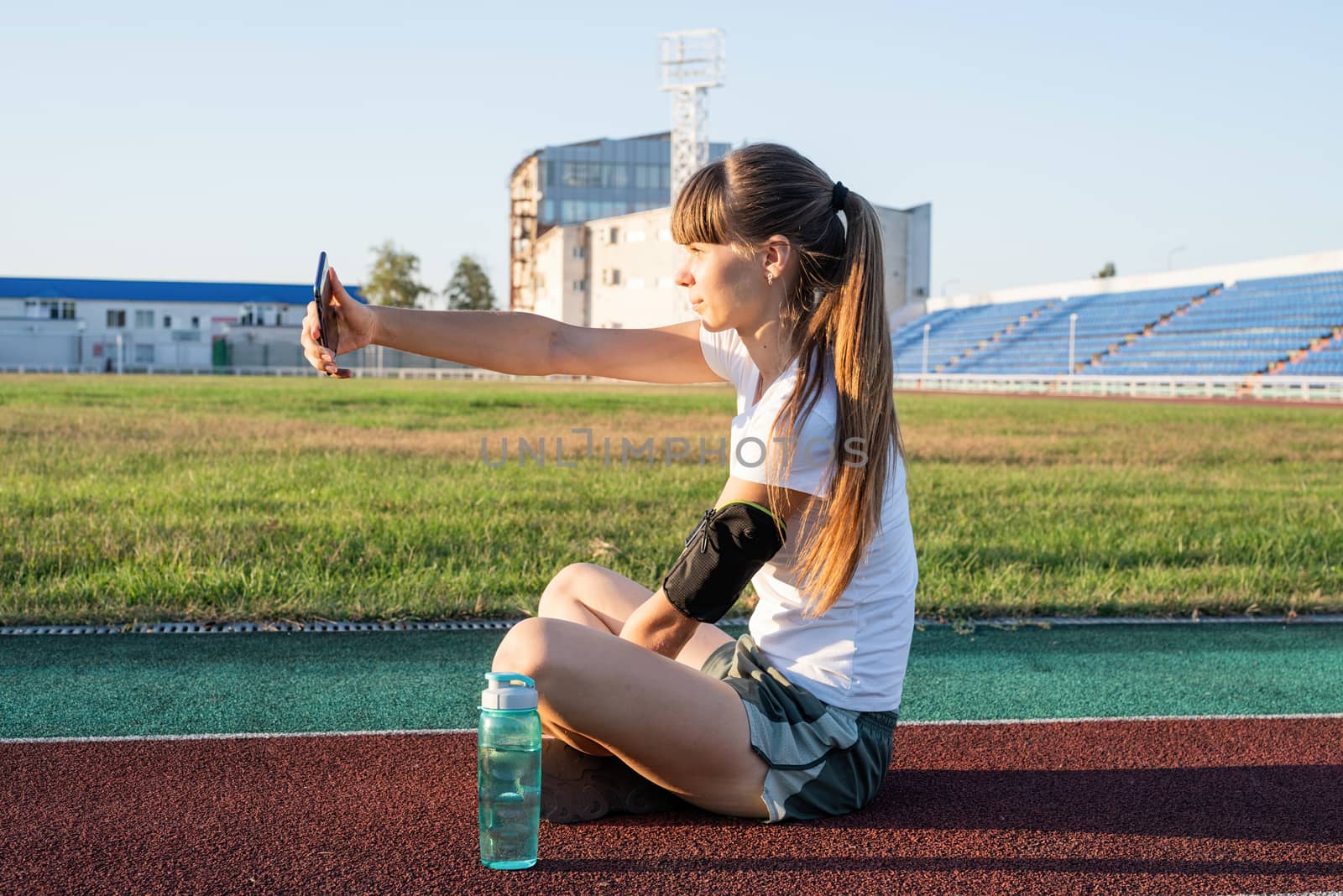 Active lifestyle. Teen girl making selfie at the stadium after workout drinking water