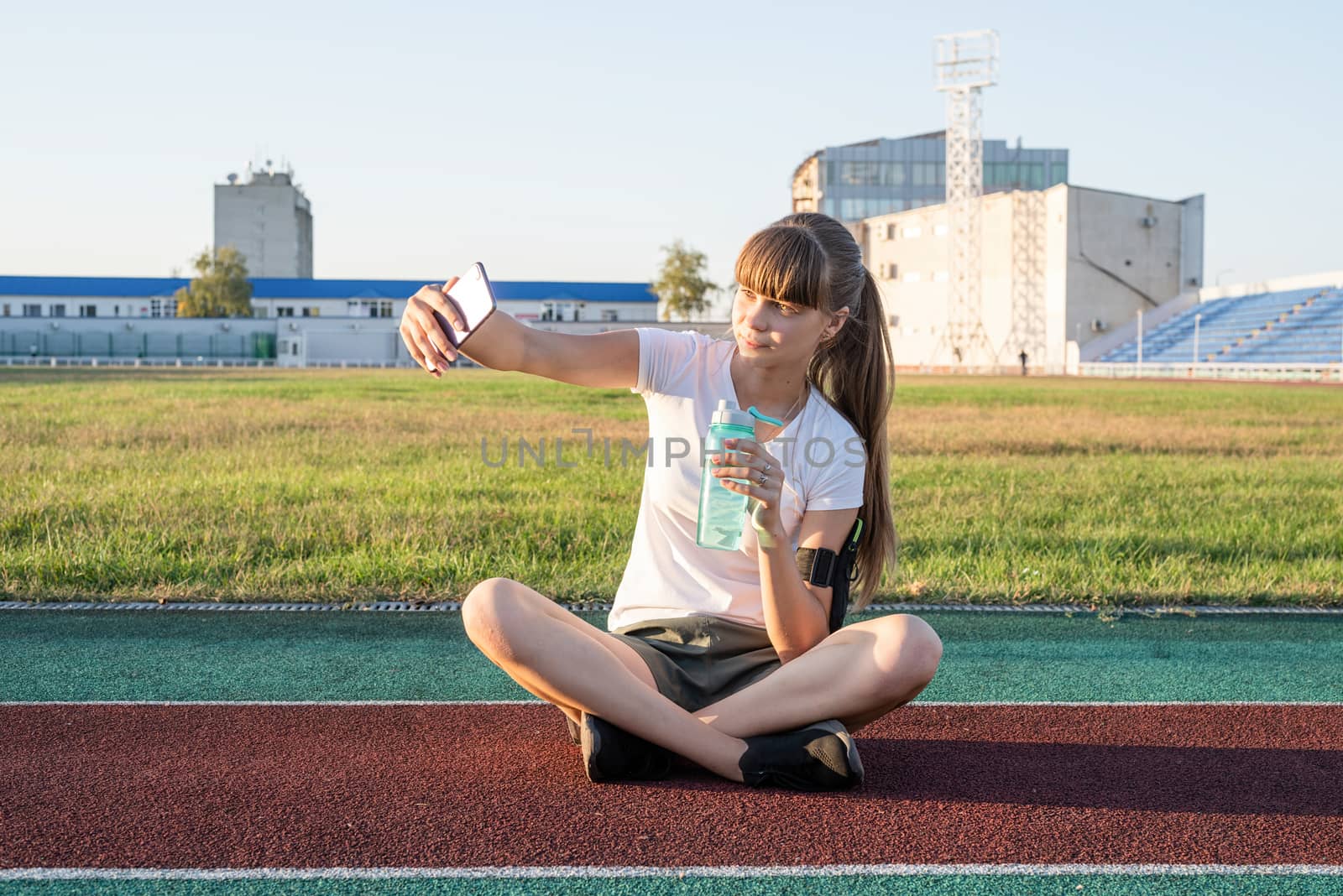 Teen girl making selfie at the stadium after workout drinking water by Desperada