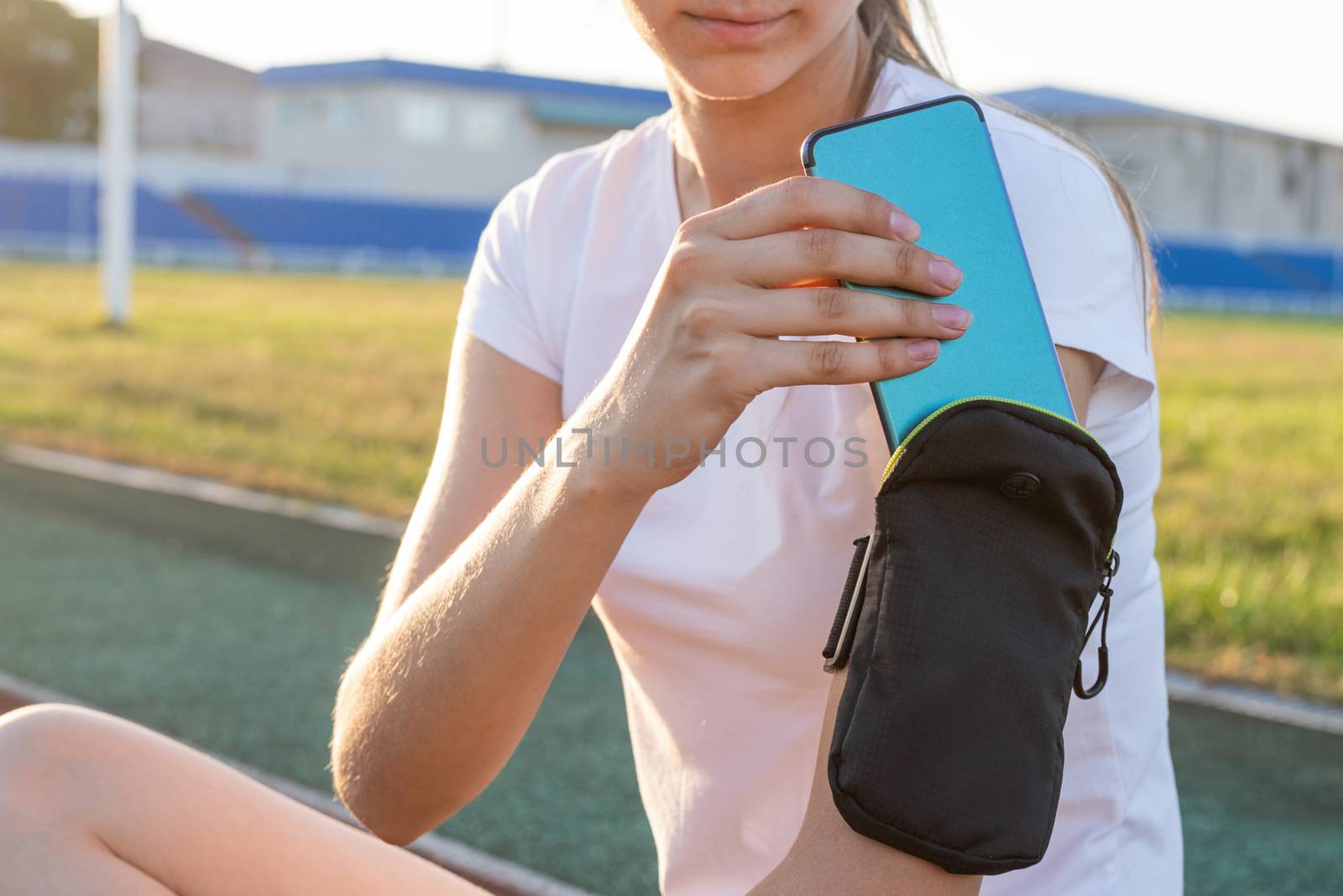 Sports and fitness. Teenage girl sitting at the stadium after working out putting her mobile phone to the pocket