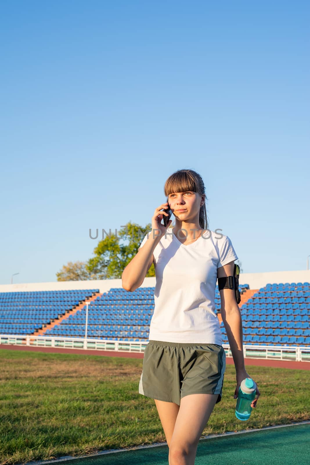 Young sports woman talking on the phone at the stadium by Desperada
