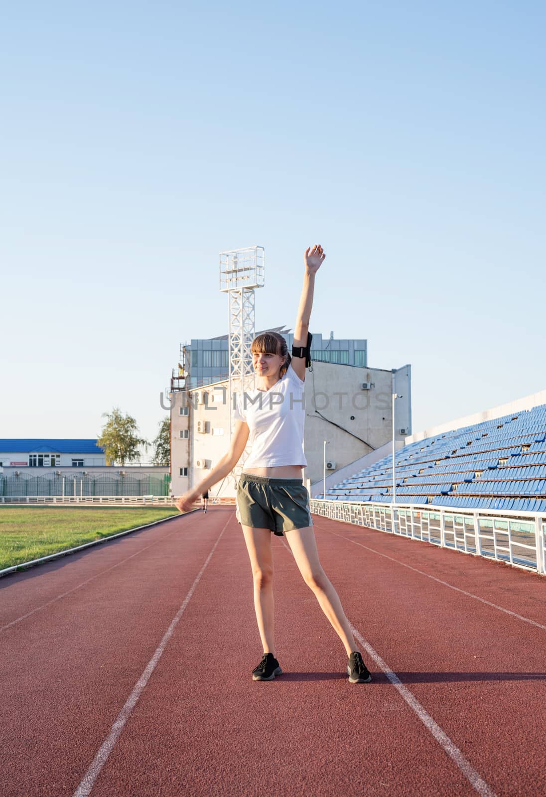 Young sports girl standing on the track rising her arms by Desperada