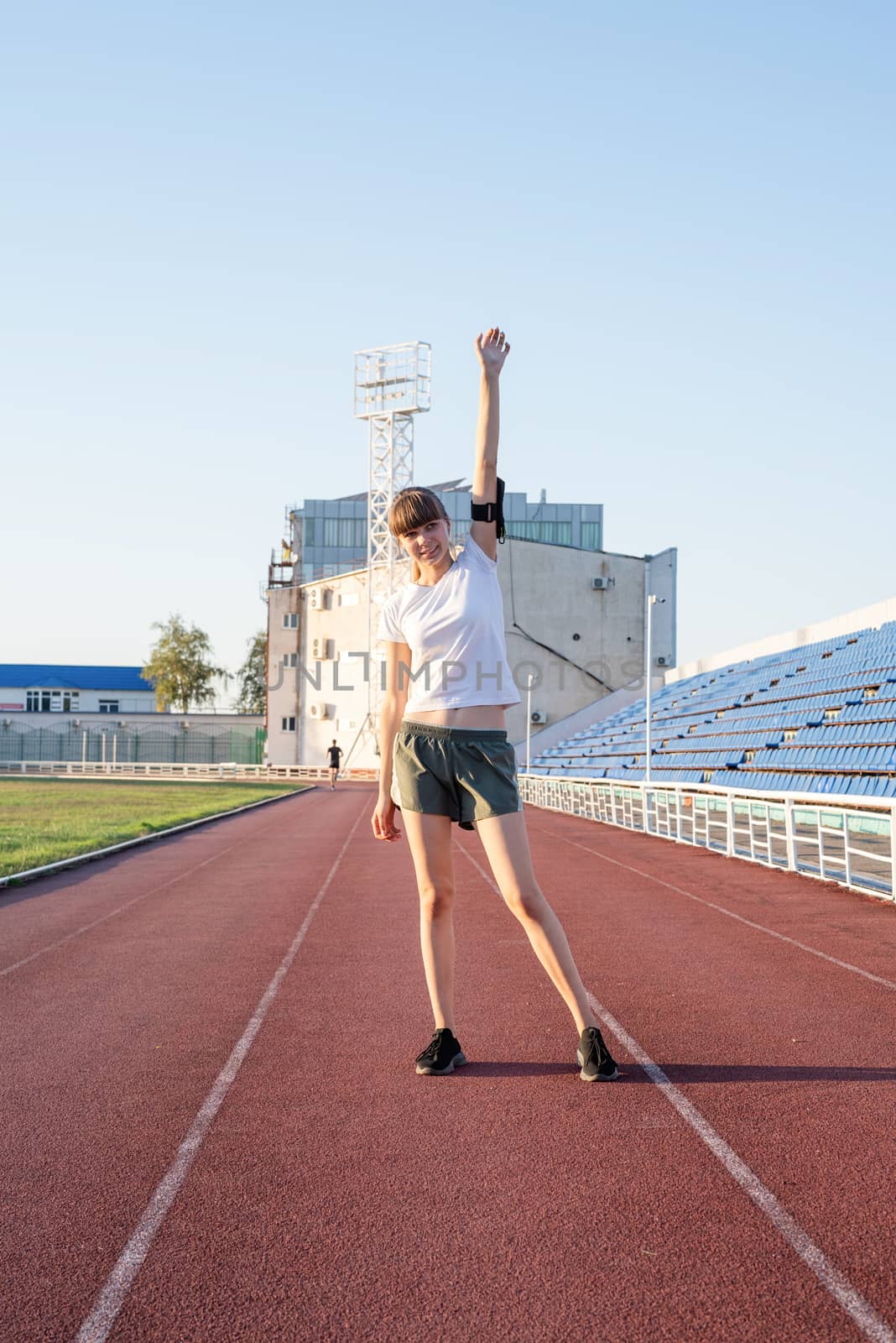 Young sports girl standing on the track rising her arms by Desperada